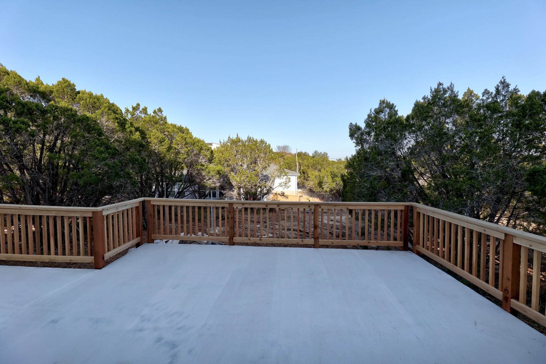 A deck with a wooden railing and a view of a wooded area.