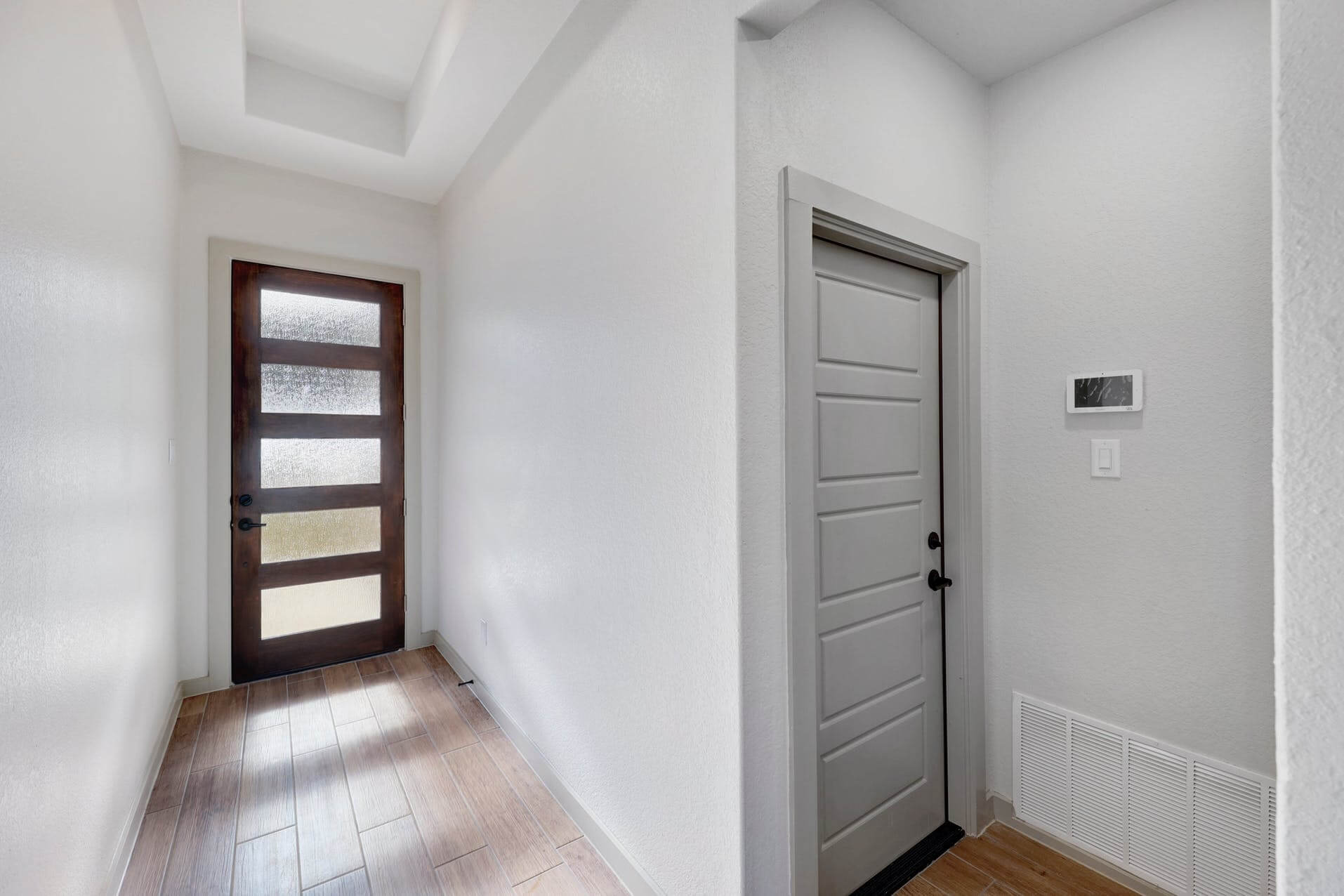 A hallway with a white door and hardwood floors.